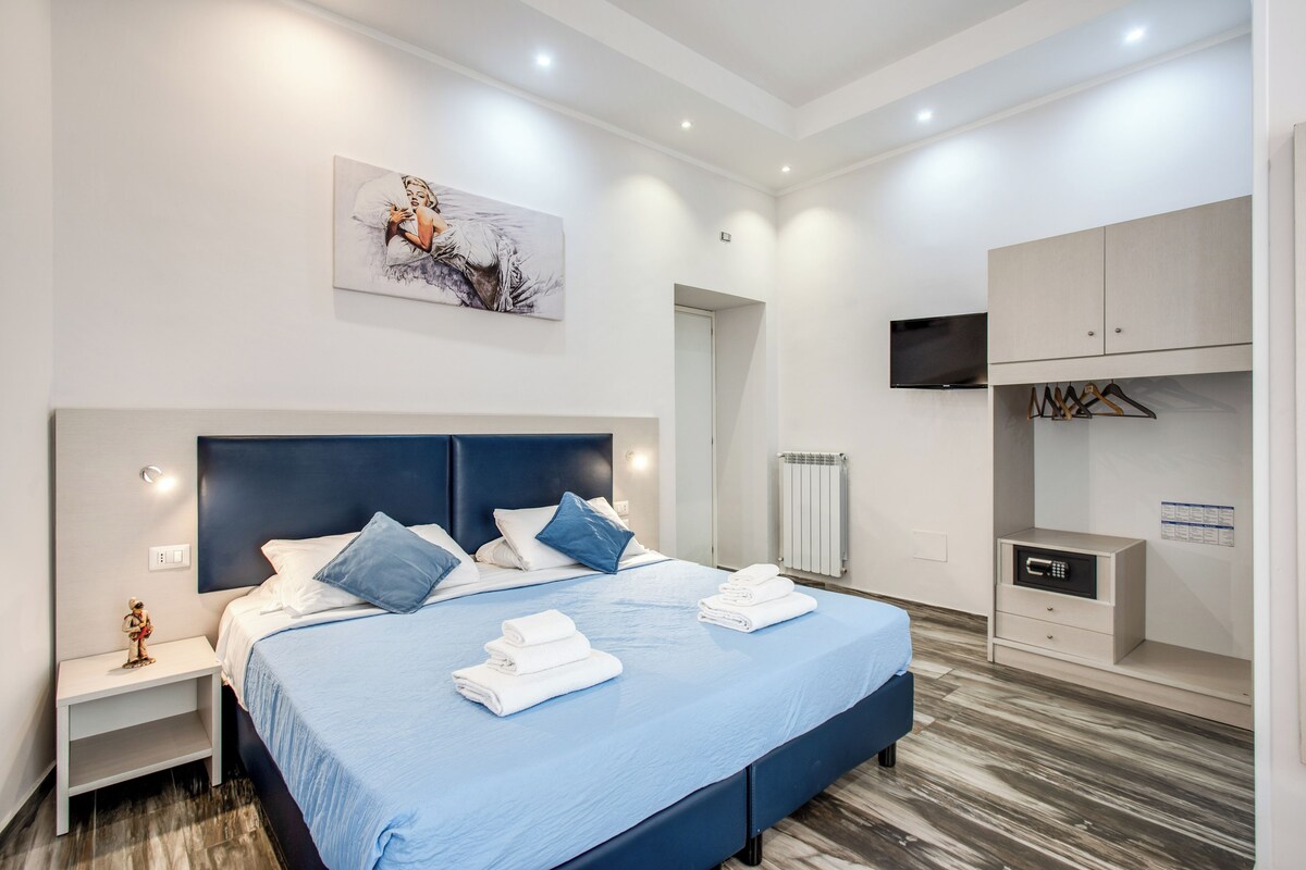 A modern hotel room with a large bed, a nightstand, a dresser, and a television.
