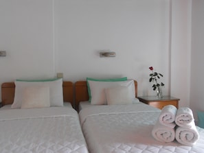 Habitación de hotel con dos camas, cada una con ropa de cama blanca y almohadas verdes, una mesita de noche con un jarrón de flores y toallas enrolladas sobre la cama.