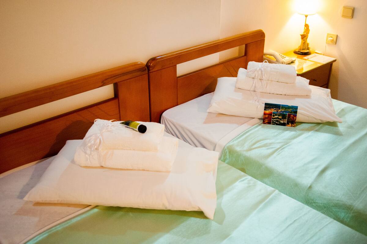 Quarto de hotel com duas camas, cada uma com toalhas brancas dobradas e um livro.