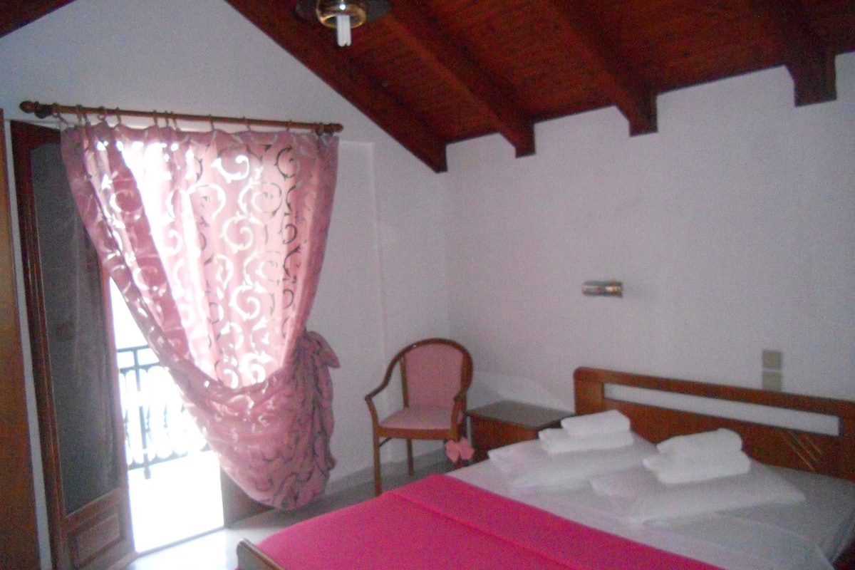 Um quarto com cama, cadeira e janela com cortina.