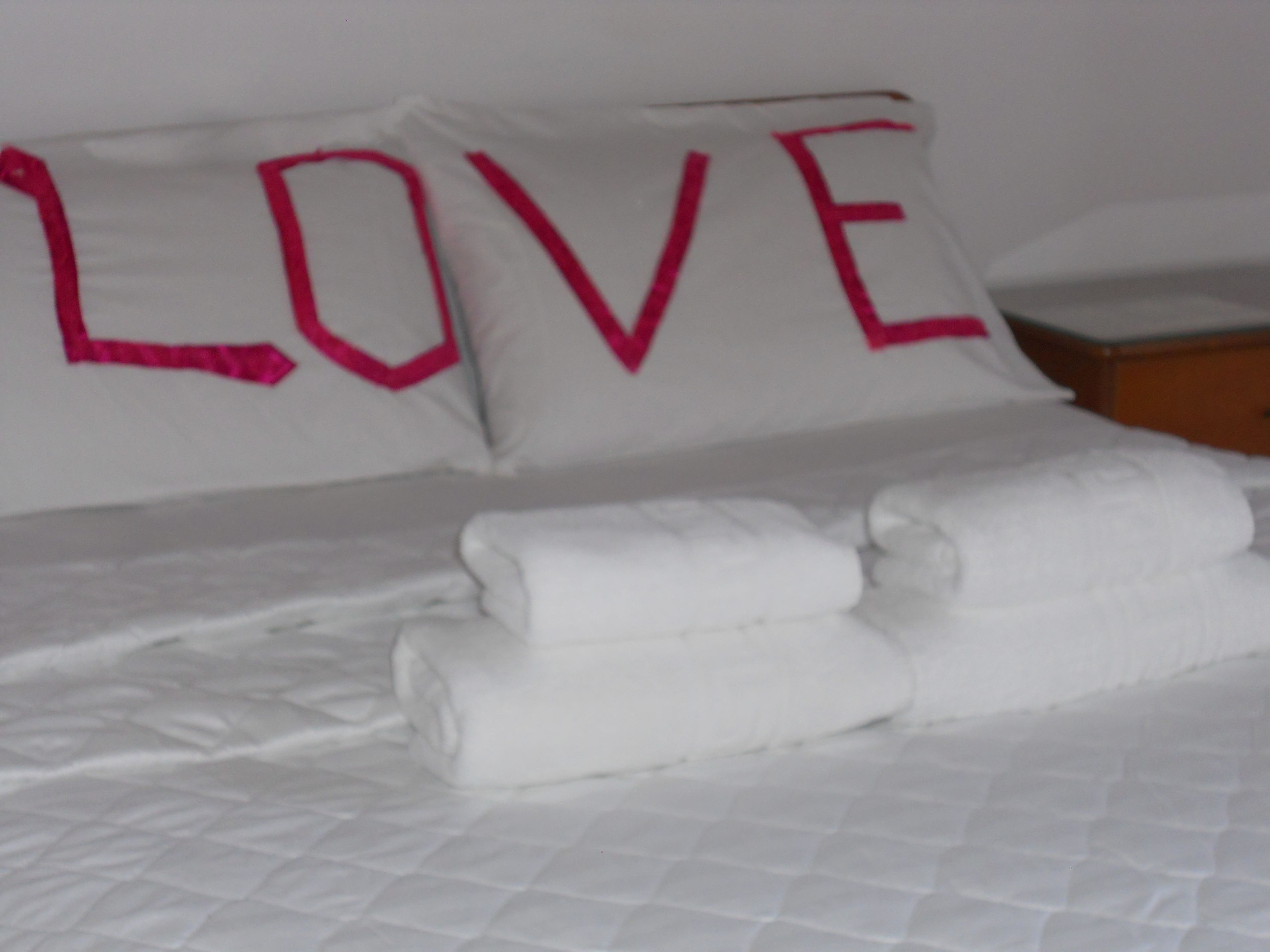 A bed with white bedding and two pillows with the word "LOVE" in pink letters.