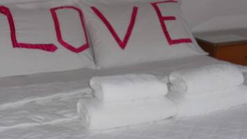 A bed with white bedding and two pillows with the word "LOVE" in pink letters.