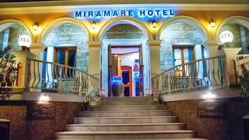 The exterior of Miramare Hotel with a grand entrance, a staircase, and illuminated signage.