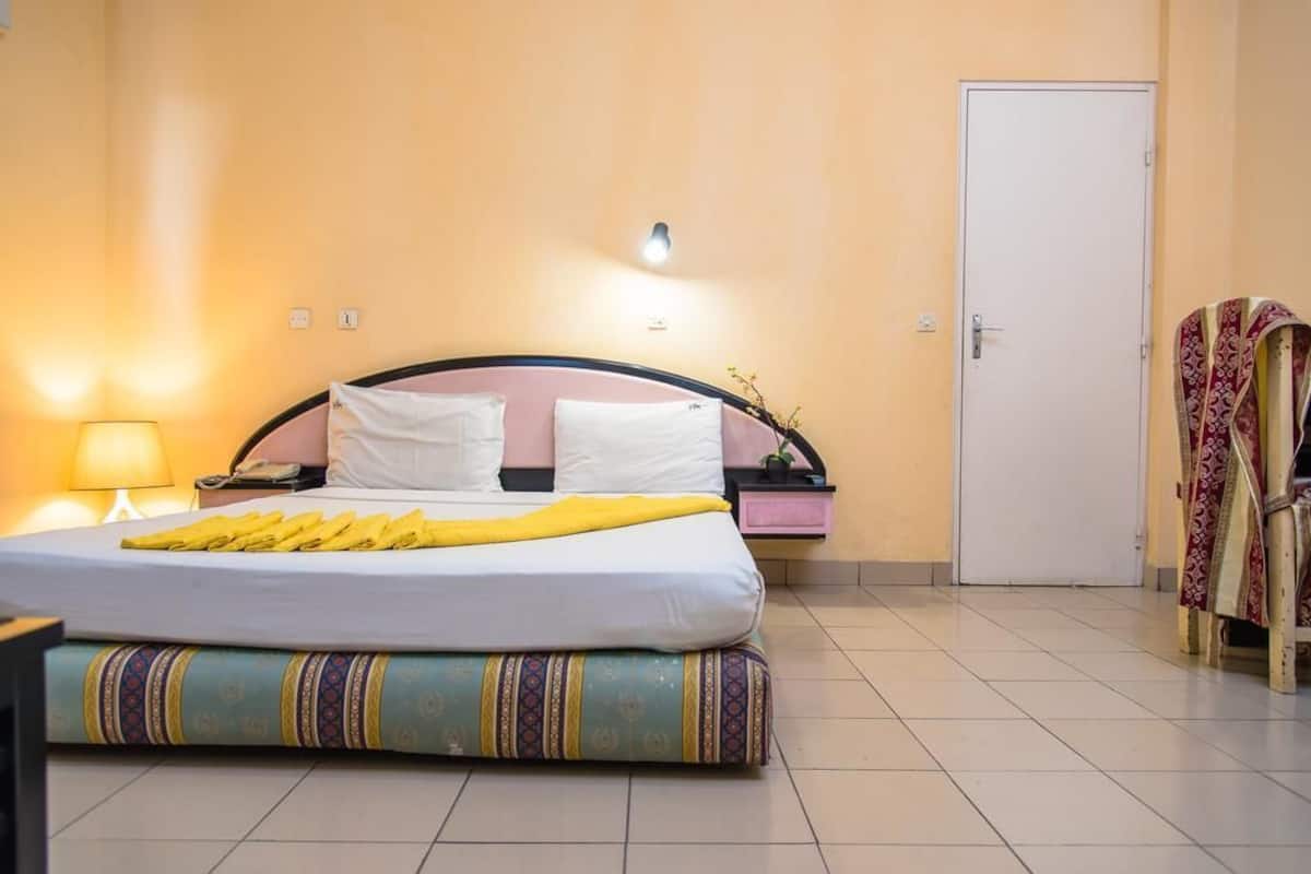A hotel room with a bed, bedside table, lamp, and a door.