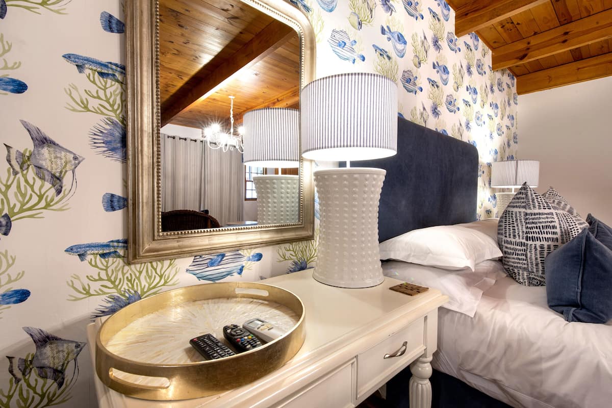 A bedroom with a bed, a bedside table with a lamp, a mirror, and a decorative wall with fish patterns.