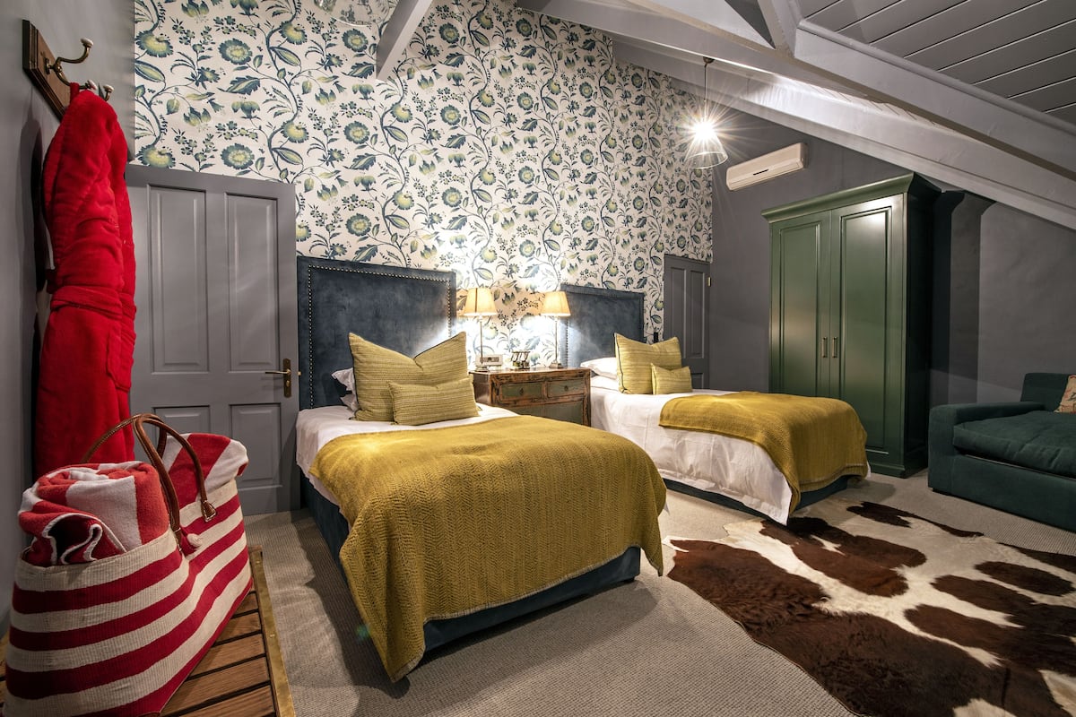 A bedroom with two beds, a large mirror, a red bag, and a green wardrobe.