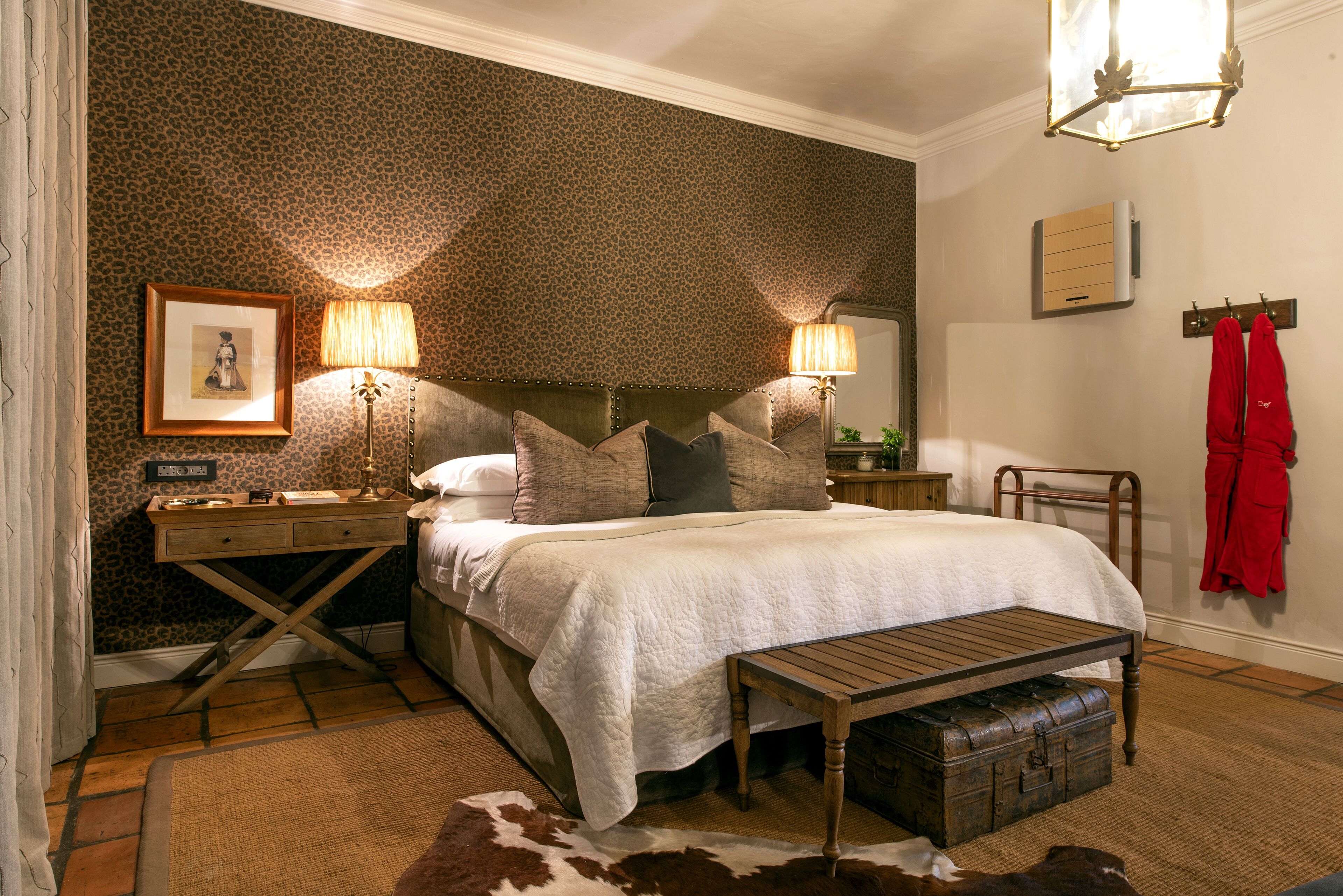 A bedroom with a bed, two bedside tables, a lamp, a coat rack, and a trunk.