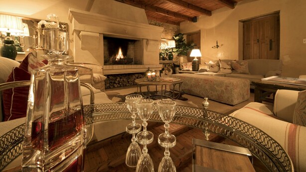 A cozy living room with a fireplace, a round coffee table with wine glasses, and comfortable seating. - Avondrood Guest House (Franschhoek)