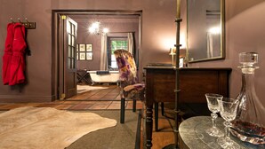 A room with a wooden floor, a fur rug, a chair, a table with glasses, and a mirror. - Avondrood Guest House (Franschhoek)