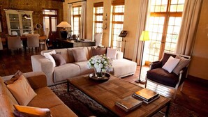 A cozy living room with a sofa, armchair, and coffee table. There is a dining area in the background with a table and chairs. - Avondrood Guest House (Franschhoek)