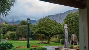 A garden with a lawn, chairs, a table, and a statue. - Avondrood Guest House (Franschhoek)