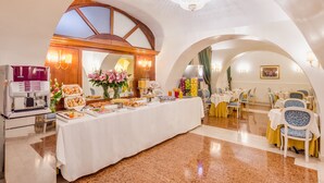 Montaje de un bufé de desayuno con una máquina de café, diversas opciones de comida y un candelabro en una sala amplia con techos abovedados y suelo pulido.