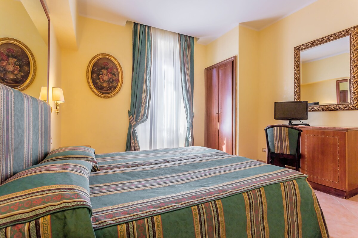 Una habitació d'hotel amb llit, escriptori, cadira, televisió i mirall.