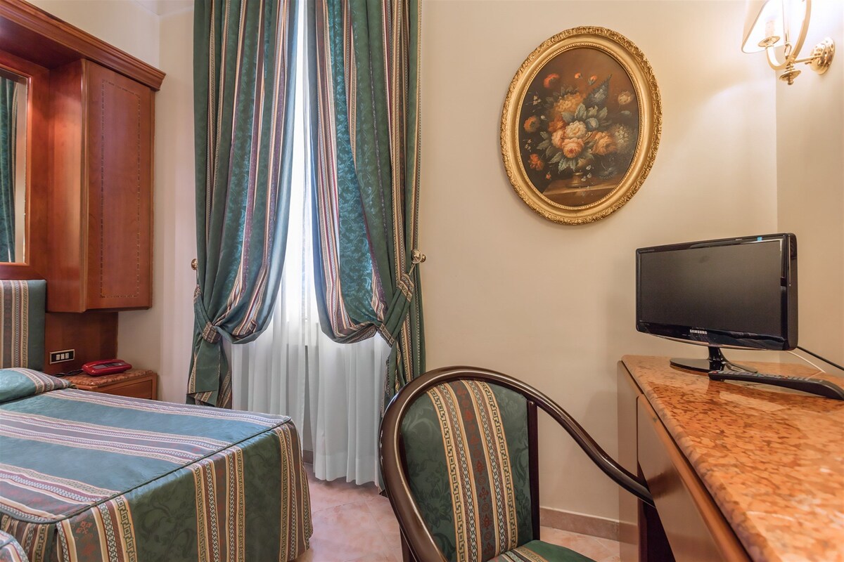 Habitació d'hotel amb dos llits, televisió, escriptori, cadira, armari i un quadre a la paret.