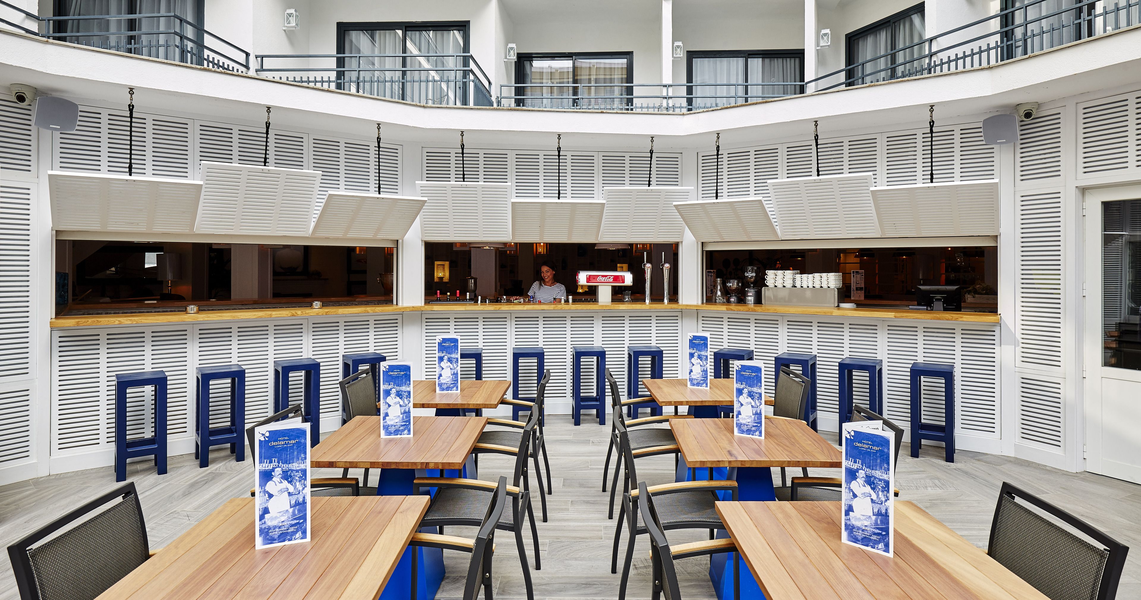 A spacious indoor dining area with multiple wooden tables and blue chairs, featuring a central bar area with a counter and stools.