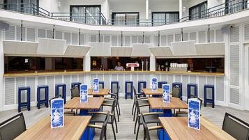 A spacious indoor dining area with multiple wooden tables and blue chairs, featuring a central bar area with a counter and stools.