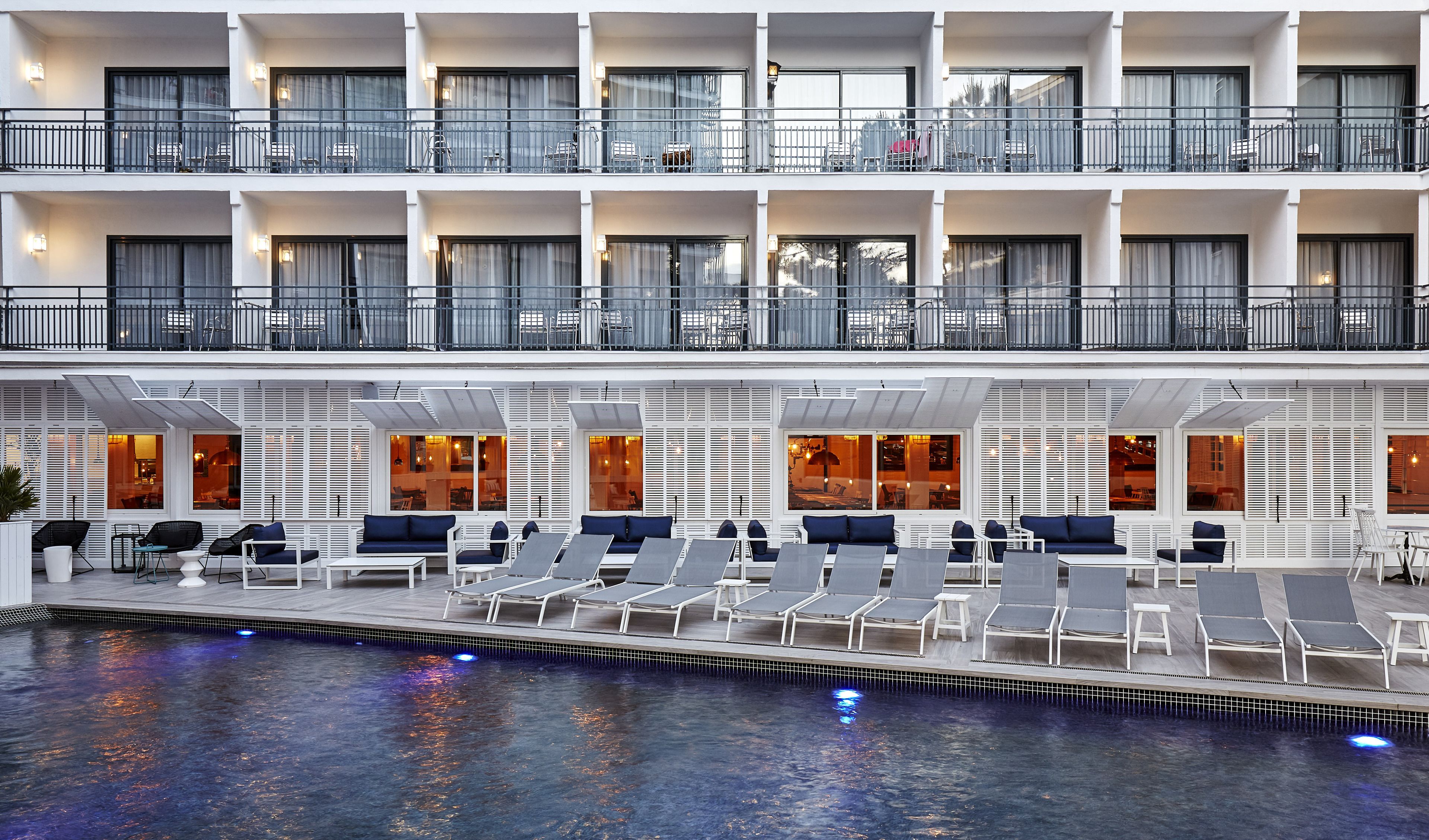 Un hôtel à plusieurs étages doté de balcons, d’un espace piscine avec des chaises longues et d’un restaurant avec de grandes fenêtres.
