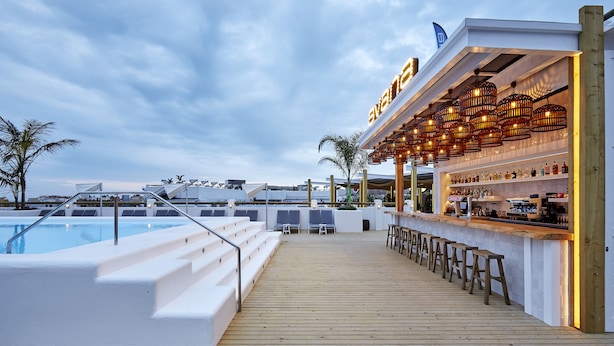 Une terrasse avec une piscine, un bar et des espaces pour s’asseoir.