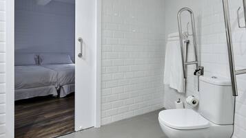 Ett modernt badrum med vita, rektangulära kakelplattor, en vit toalett och en dusch med kromad blandare.