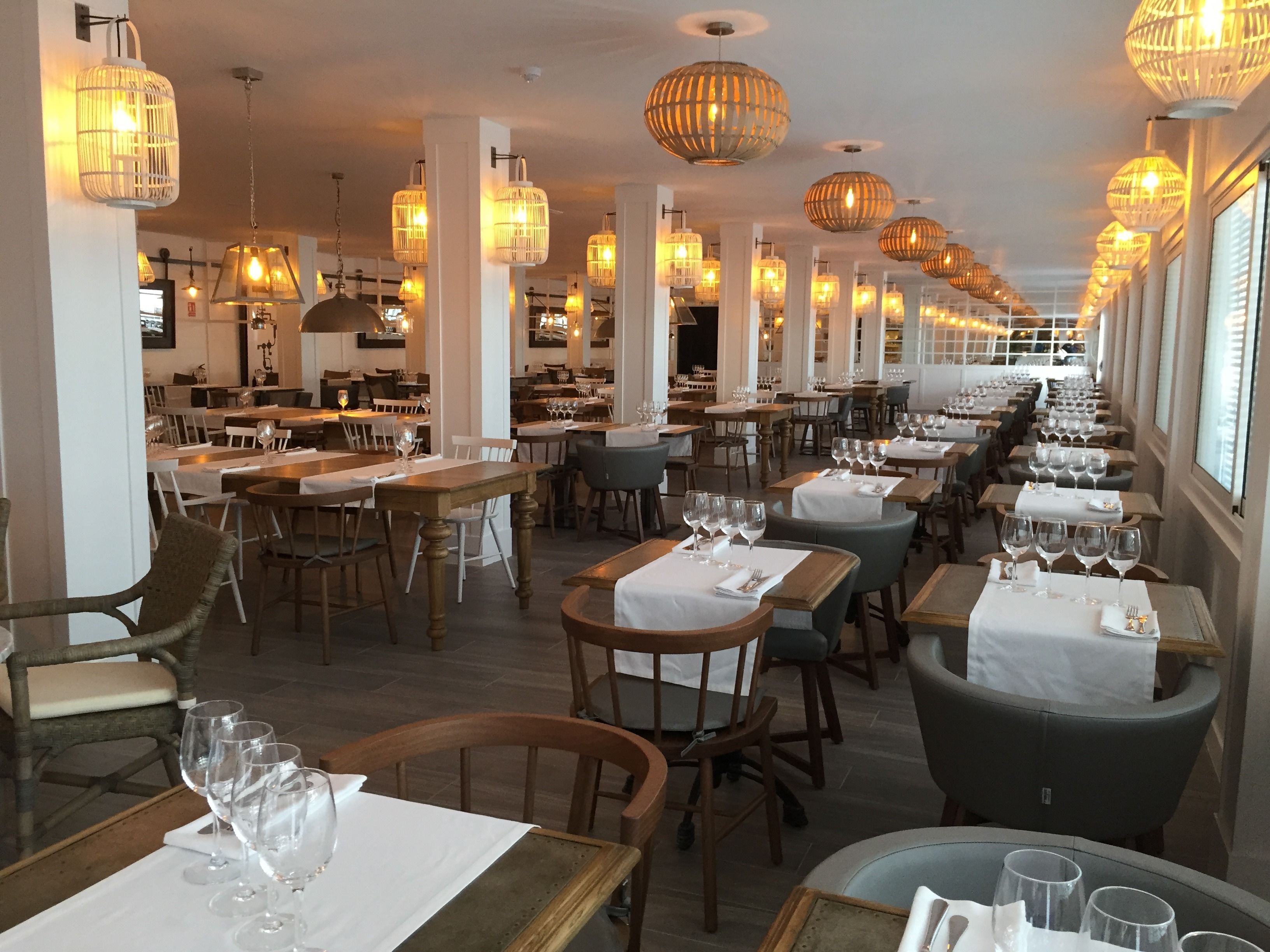 Un restaurante con varias mesas y sillas, iluminación cálida y una barra alargada.