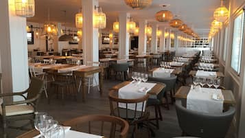 Un restaurante con varias mesas y sillas, iluminación cálida y una barra alargada.