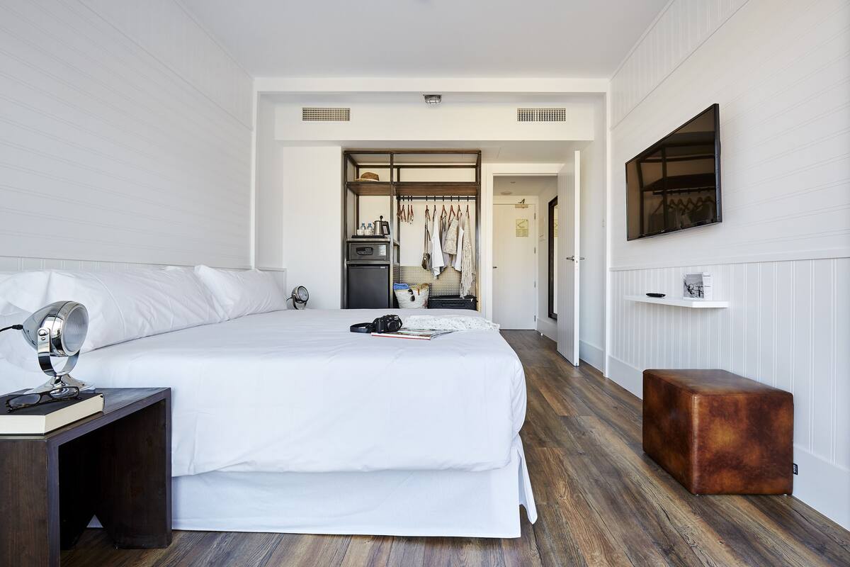 Une chambre à coucher bien rangée, avec un grand lit, une table de chevet et un petit tabouret.