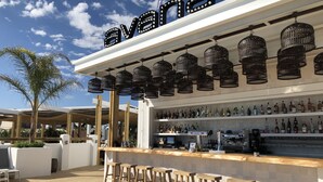 Un espace bar extérieur doté d’une terrasse en bois, de tabourets de bar et d’une variété de bouteilles d’alcool.