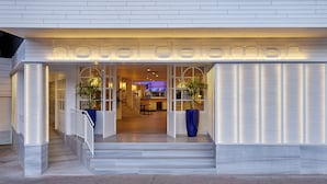L’entrée d’un hôtel au design moderne, avec un escalier menant au hall d’accueil et deux grands plants en pot de chaque côté de l’entrée.