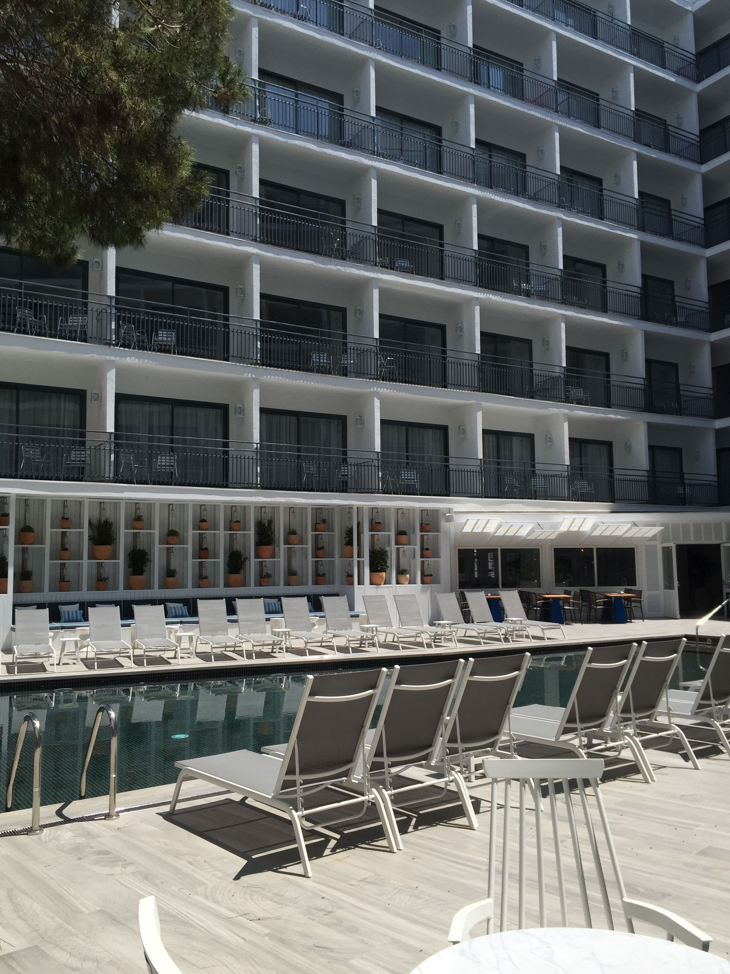 A hotel with a pool area featuring sun loungers and a seating area with tables and chairs.