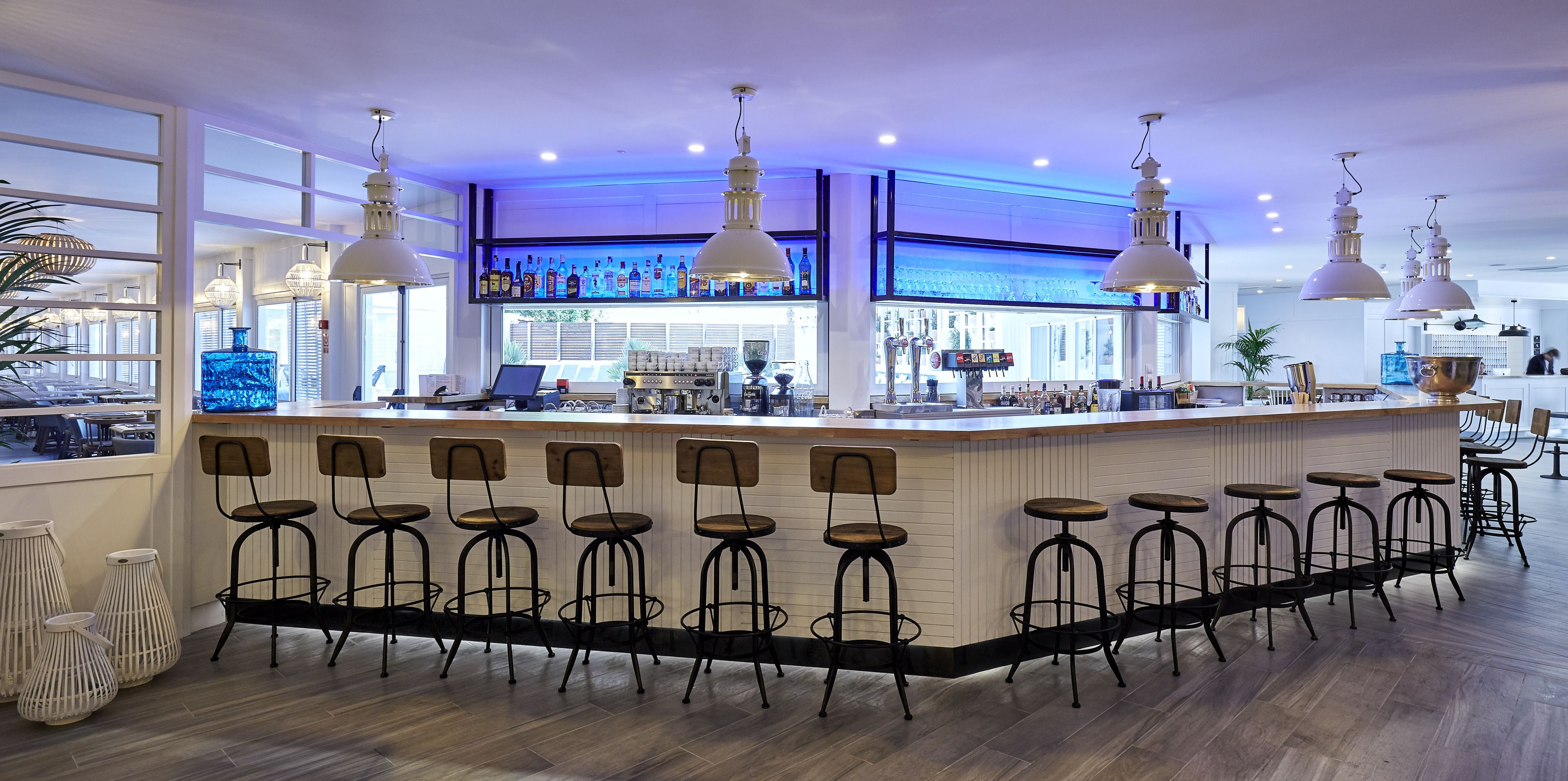 A bar area with a long counter, multiple stools, and hanging pendant lights.