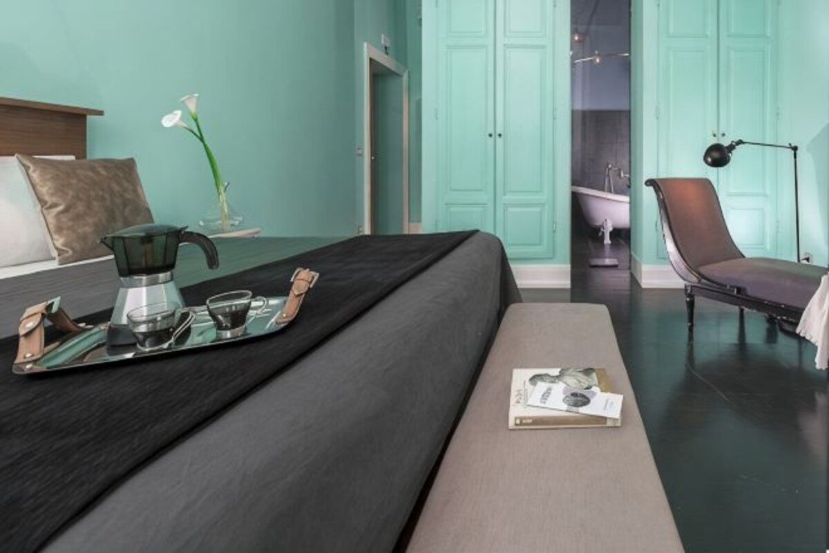 A modern hotel room with a bed, a bedside table with a tray, a chair, and a view of a bathroom.