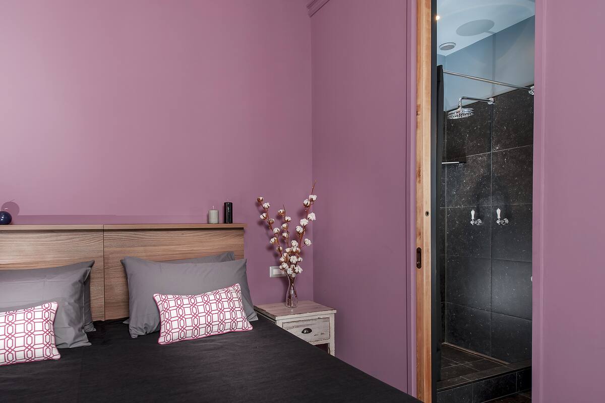 A bedroom with a bed, pillows, a nightstand, a vase with flowers, and a shower area.