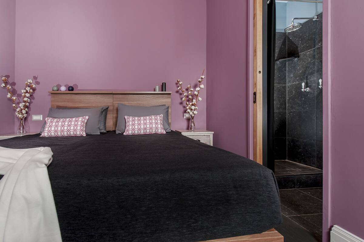 A bedroom with a bed, two nightstands, a wooden headboard, and a bathroom with a shower.