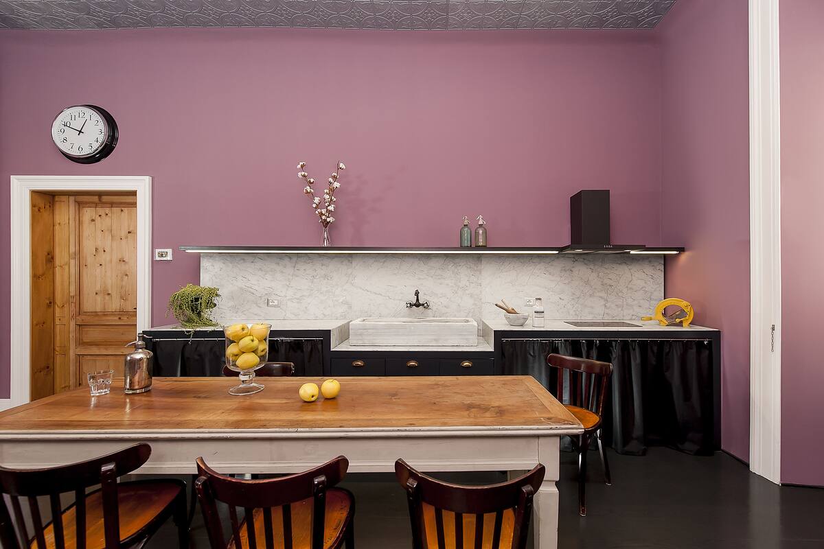 A kitchen with a wooden table, chairs, a marble countertop, and a purple wall.