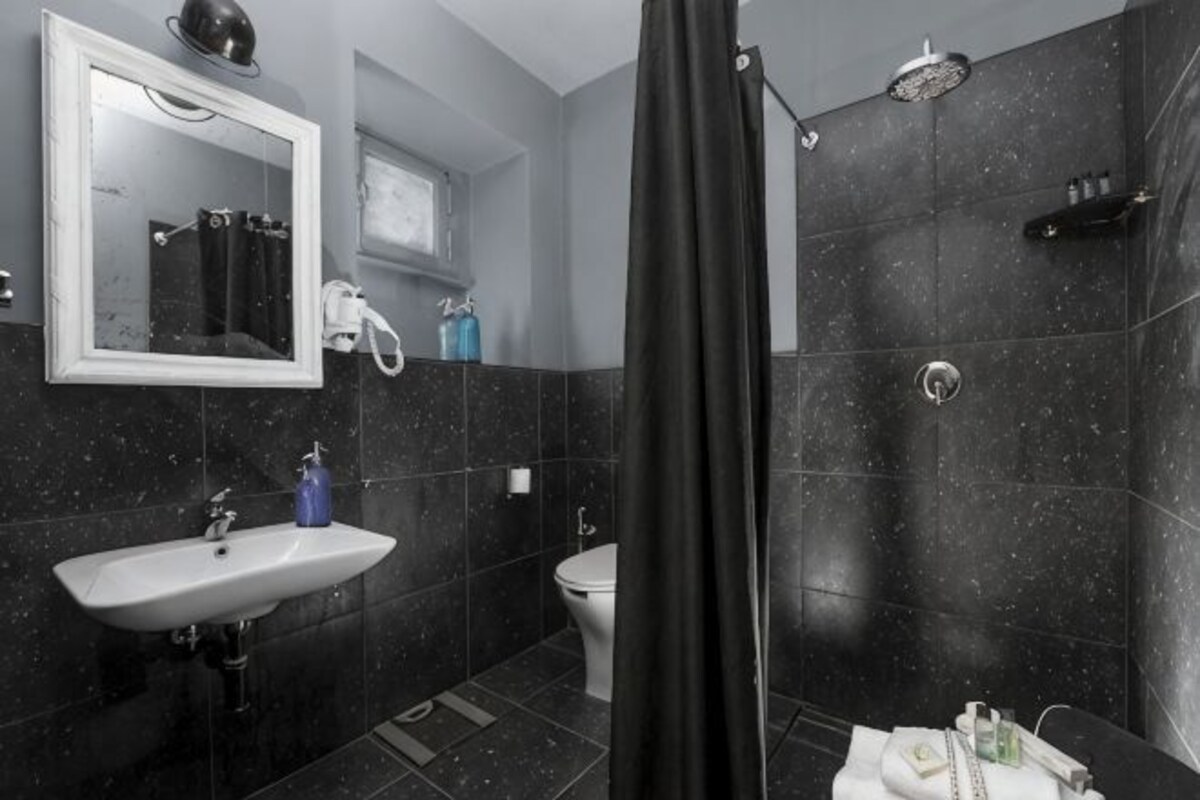 A bathroom with a sink, toilet, mirror, shower, and tiled walls.