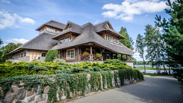 A large, rustic house with a thatched roof, surrounded by lush greenery and a lake view. - Porto Resort (Lilaste)