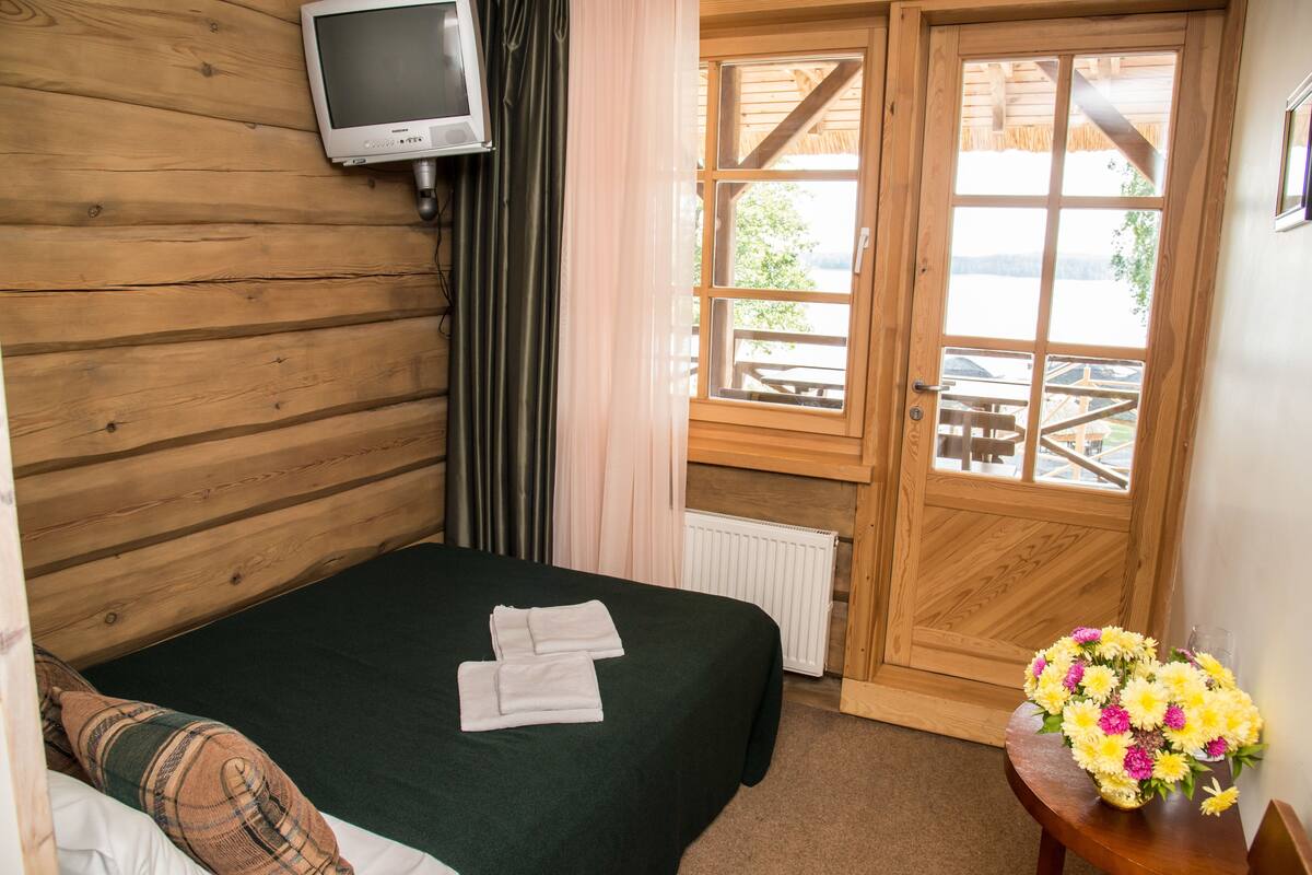 Una habitación de madera con una cama, un televisor, una ventana y una mesa con flores.