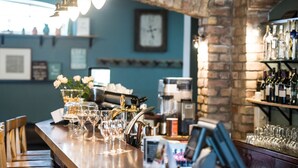 A bar area with a wooden counter, glasses, and bottles. There is a clock on the wall and a coffee machine in the background. - Porto Resort (Lilaste)