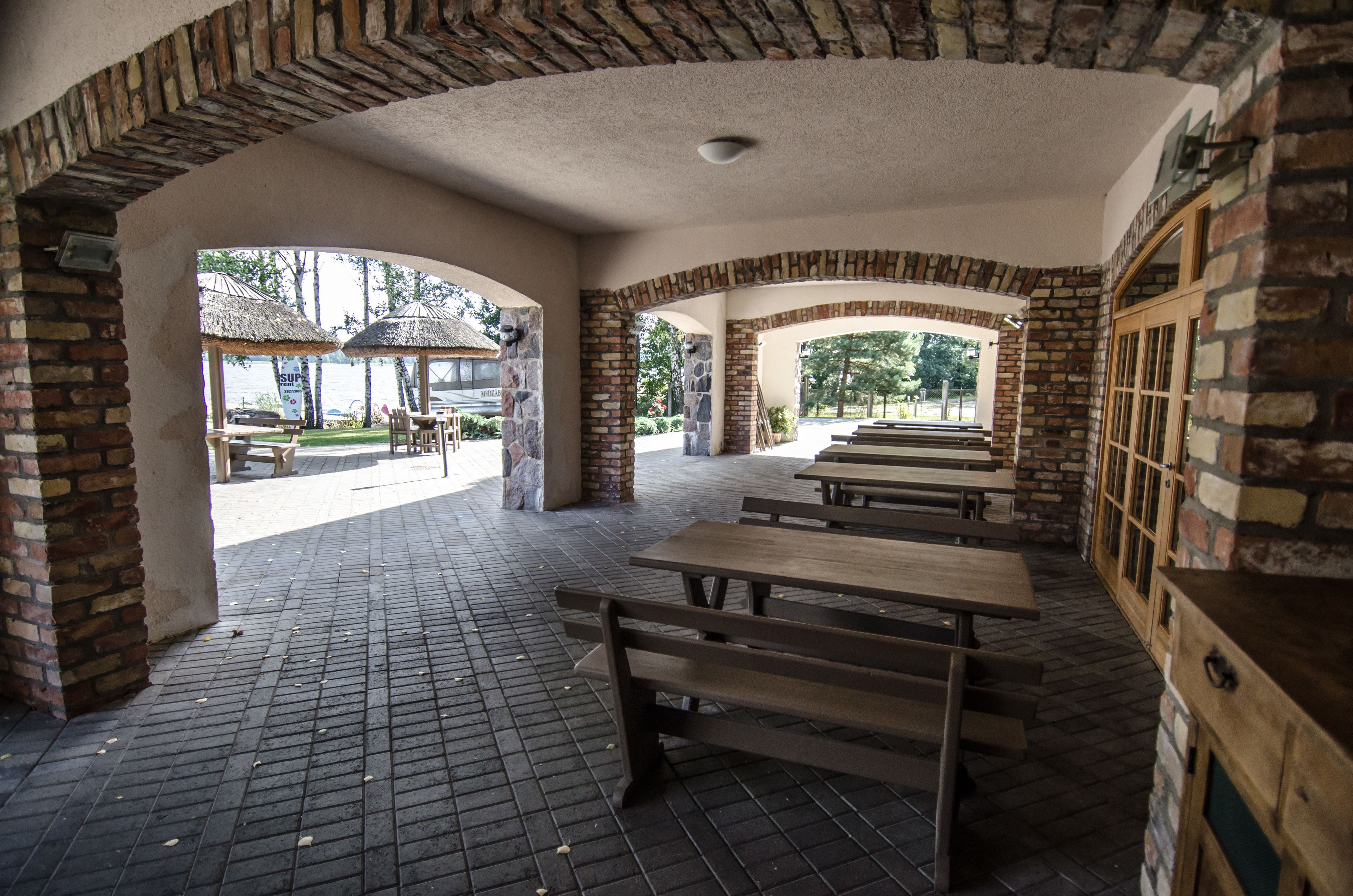 An outdoor patio area with brick walls, wooden benches, and thatched umbrellas.