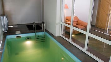A swimming pool with a glass enclosure, a towel rack, and a view of a room with a sofa and a lamp.