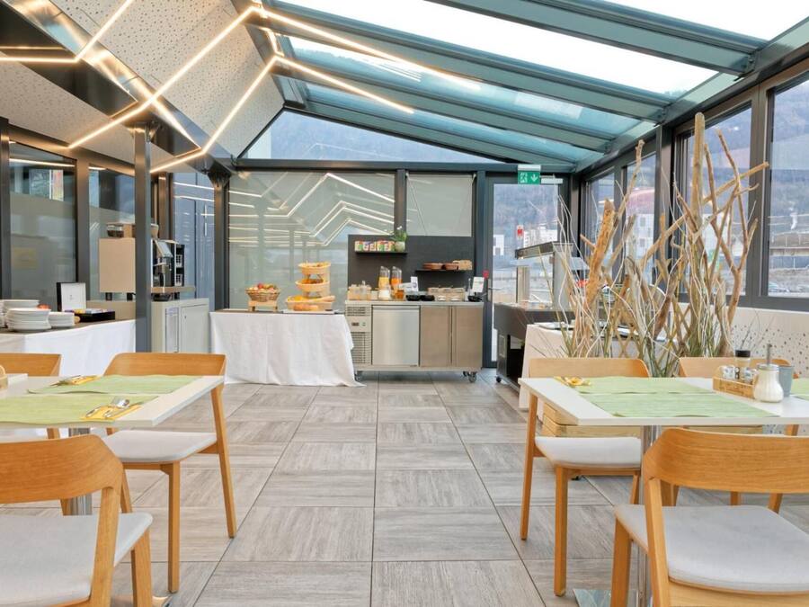 A modern restaurant with a glass ceiling, wooden chairs, and a buffet setup.