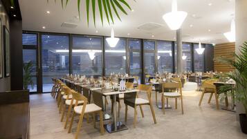 A modern dining area with multiple tables and chairs, large windows, and ceiling lights.