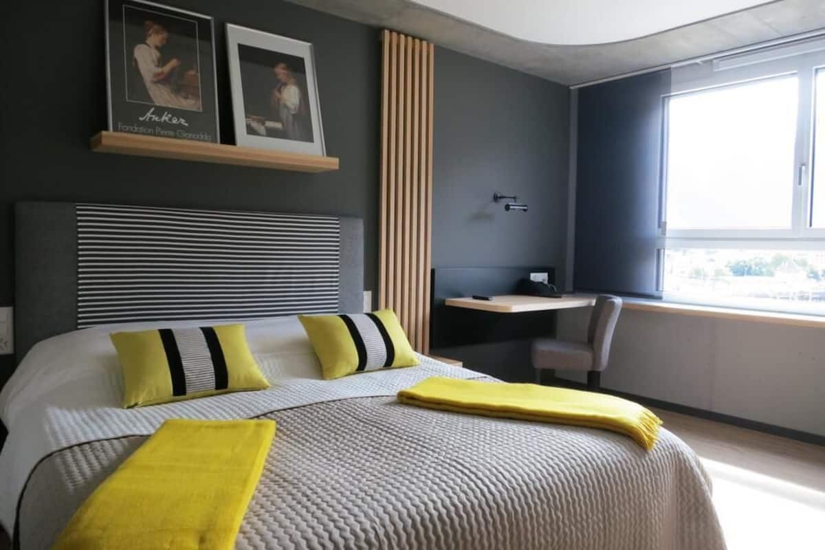 A modern hotel room with a large bed, a desk, and a window.