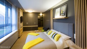 A modern hotel room with a large bed, a small seating area, and a view of the outdoors.
