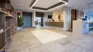 A modern reception area with a reception desk, a large potted plant, and a seating area in the background.