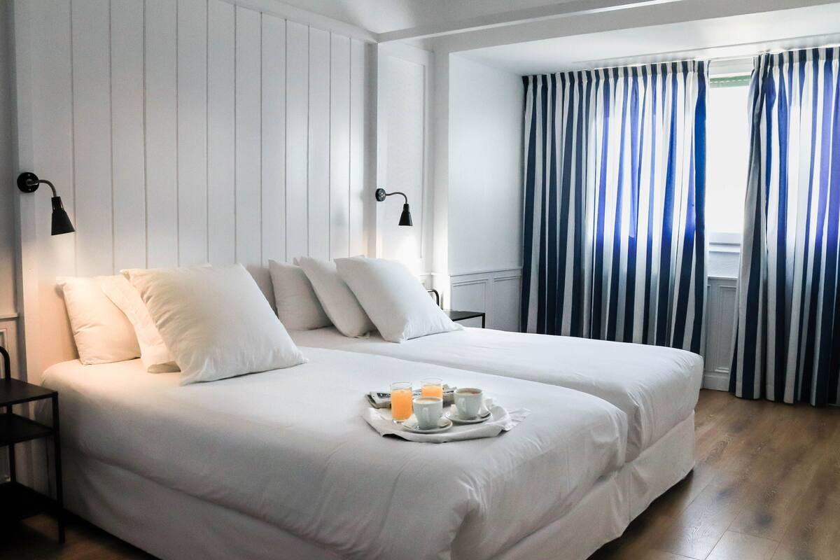 Habitación de hotel con dos camas, una bandeja con alimentos para el desayuno y una ventana con cortinas a rayas.