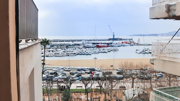 A view from a balcony overlooking a marina with boats, a beach, and a parking lot.