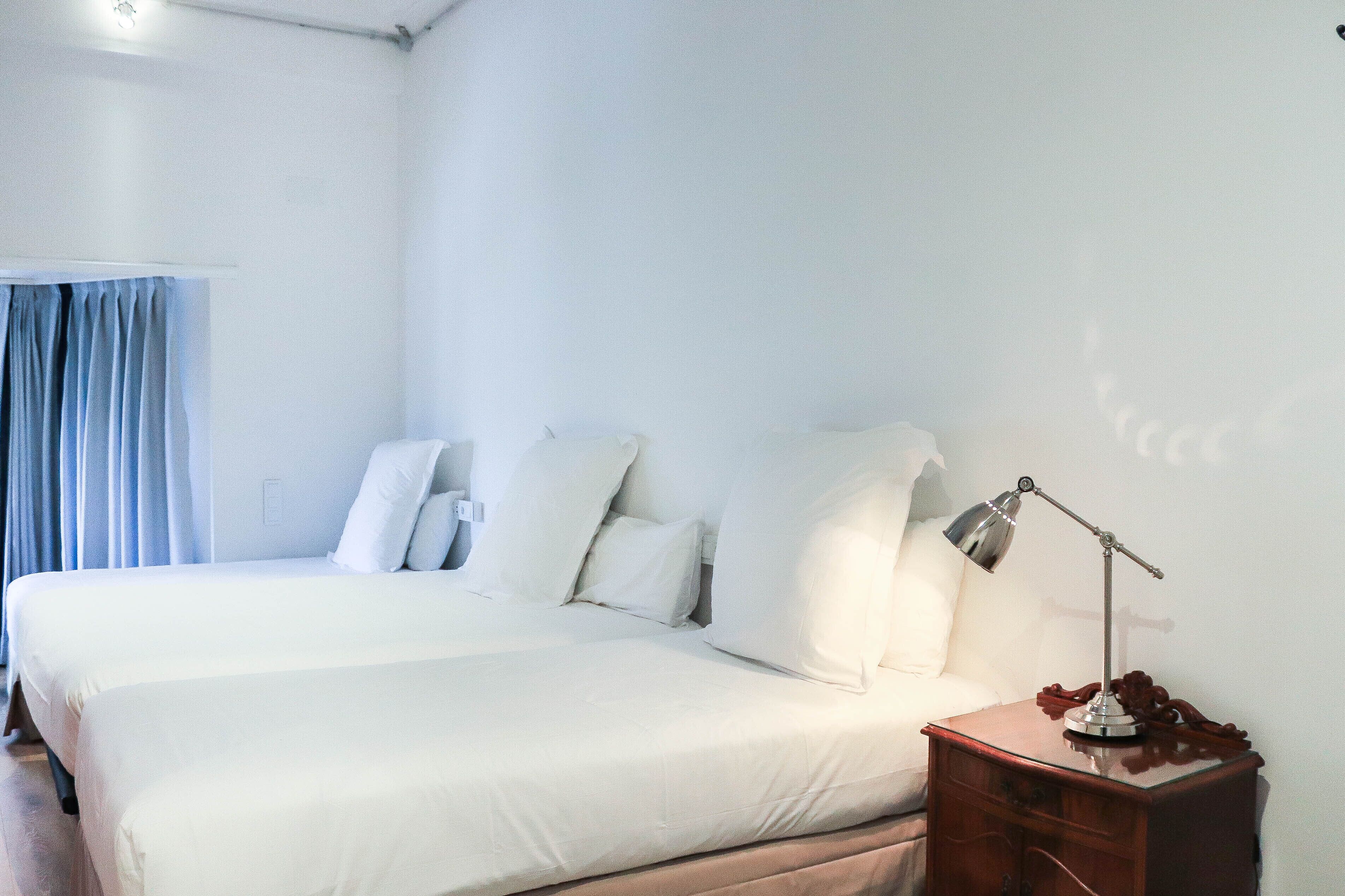 Una habitación de hotel con una cama grande, una mesita de noche con lámpara y una ventana con cortinas.