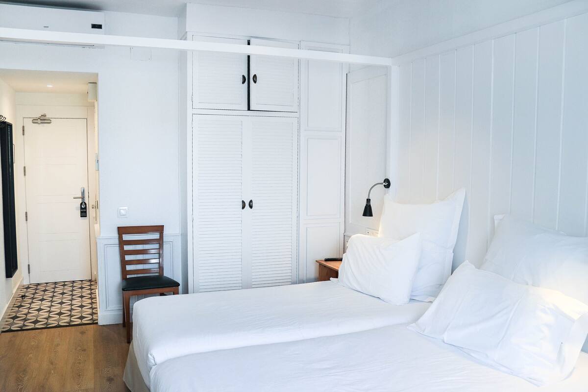 Un dormitorio con cama, una silla, un armario y una mesita de noche.