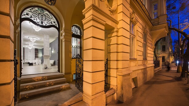 A grand entrance with steps leading to a well-lit interior, featuring a chandelier and elegant decor. - Wilson Palace by LOFT (Bratislava)